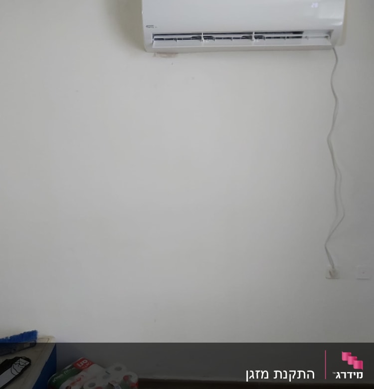 מזגן מותקן על קיר לבן עם כבל חשמל